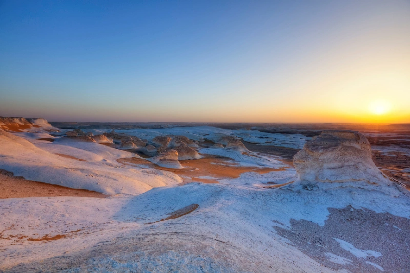 Paisaje del Desierto Blanco en Egipto al atardecer, con formaciones rocosas blancas y cielo colorido.