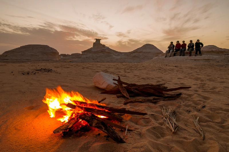 Grupo de amigos disfrutando de una fogata en el Desierto Blanco de Egipto al atardecer.