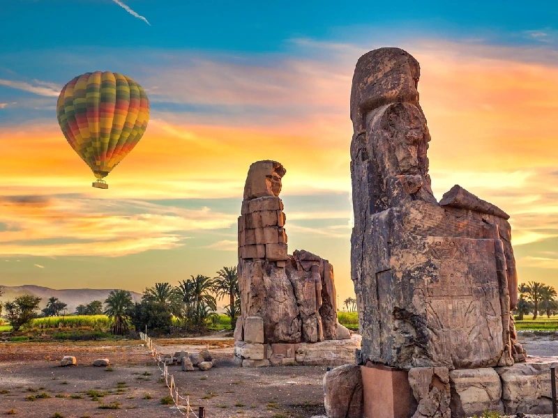 Montgolfière survolant les Colosses de Memnon dans un ciel doré à Louxor