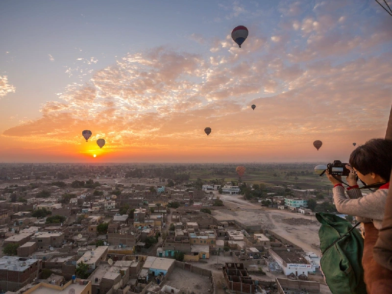 Voyageur photographiant le lever du soleil depuis la nacelle d'une montgolfière au-dessus de Louxor
