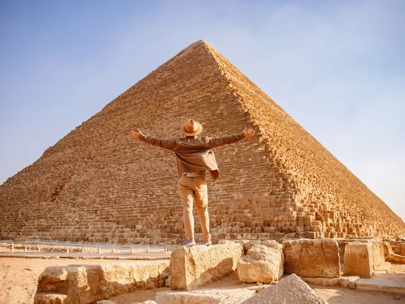 Voyageur les bras levés devant la Grande Pyramide de Gizeh