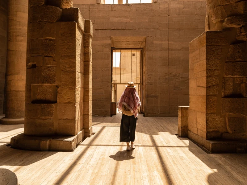 Voyageuse coiffée d'un keffieh dans la salle d'un temple égyptien baignée de lumière