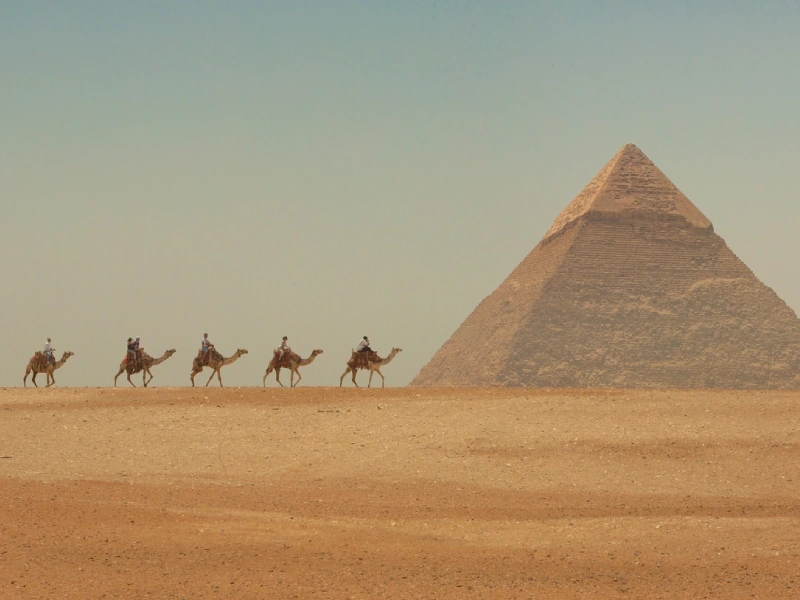 Caravane de chameaux dans le désert devant une pyramide de Gizeh