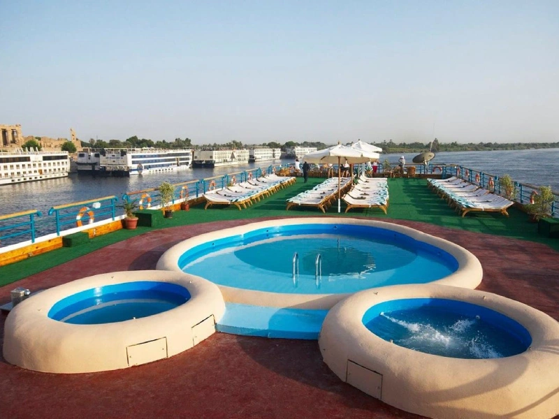Ponte di una nave da crociera sul Nilo con piscine circolari, lettini prendisole e vista panoramica sul fiume calmo