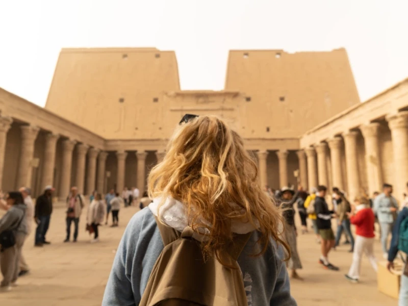 Una turista cammina verso l'imponente ingresso del Tempio di Horus a Edfu,