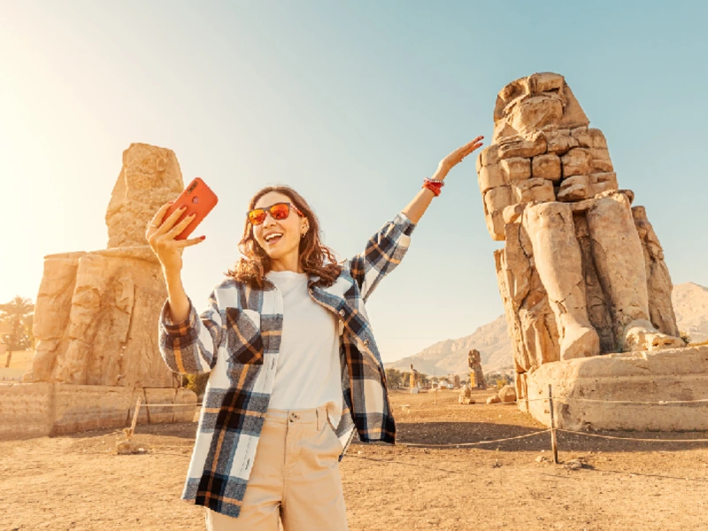 Una chica se toma selfies con los famosos dos Colosos de Memnón, enormes estatuas en ruinas del faraón Amenhotep III. Atracciones turísticas mundiales.