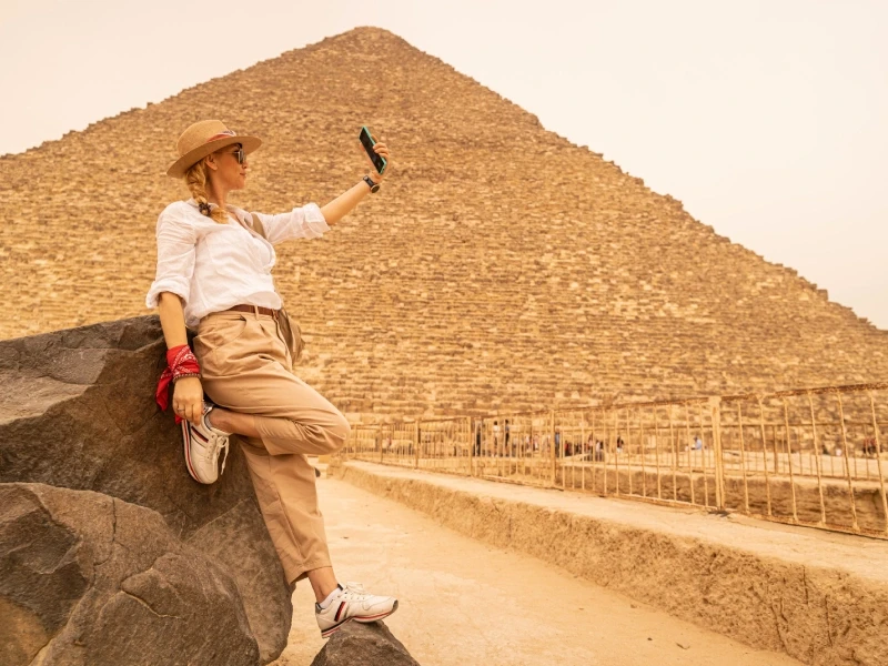 Ragazza sorridente che scatta un selfie con lo smartphone davanti alle Piramidi di Giza, Egitto.