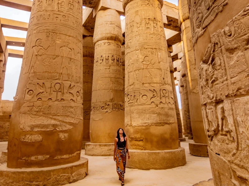 Giovane viaggiatrice esplora l'antico Tempio di Karnak a Luxor, tra maestose colonne ornate di geroglifici egizi.