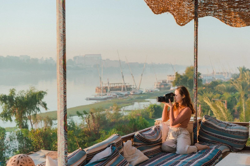 Joven sentada en una terraza y fotógrafo Nilo al atardecer en Luxor