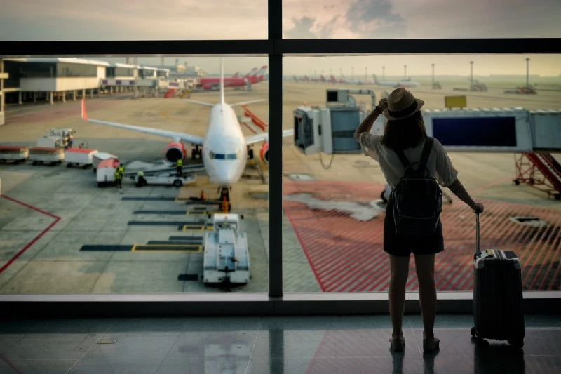 Persona de espaldas con maleta en aeropuerto mirando un avión listo para despegar