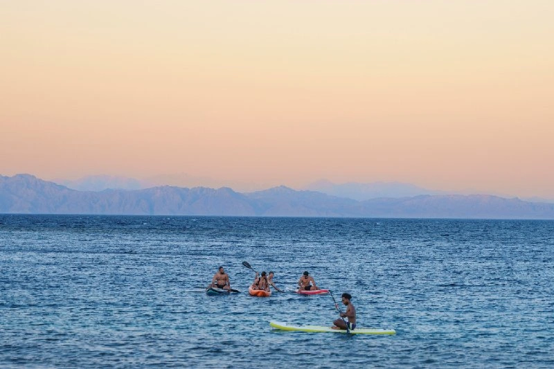 Personas practicando kayak y paddle en el Mar Rojo, en Dahab, Egipto, al atardecer.