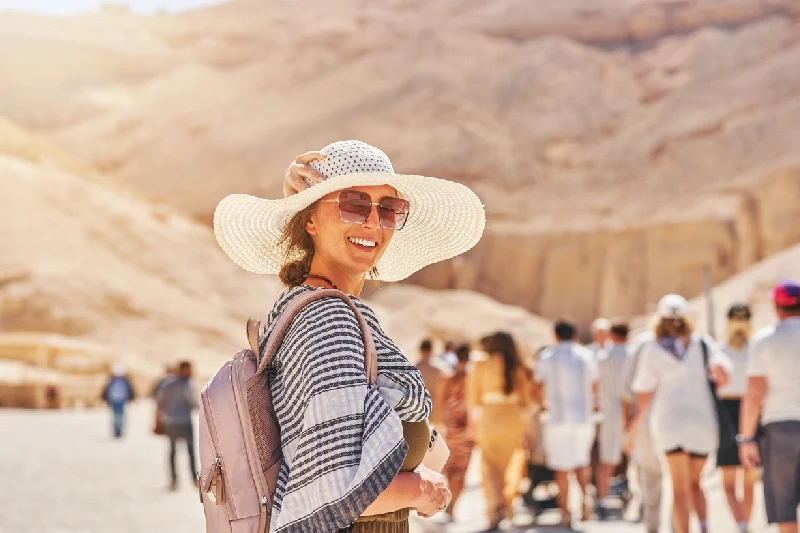 viaggiatrice sorridente con cappello e zaino durante una visita a un sito archeologico nel deserto, viaggio in egitto cosa sapere