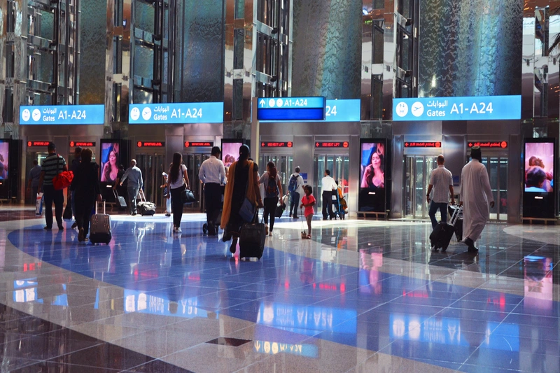Viajeros caminando hacia grandes y modernos ascensores en el vestíbulo del Aeropuerto de Dubái.