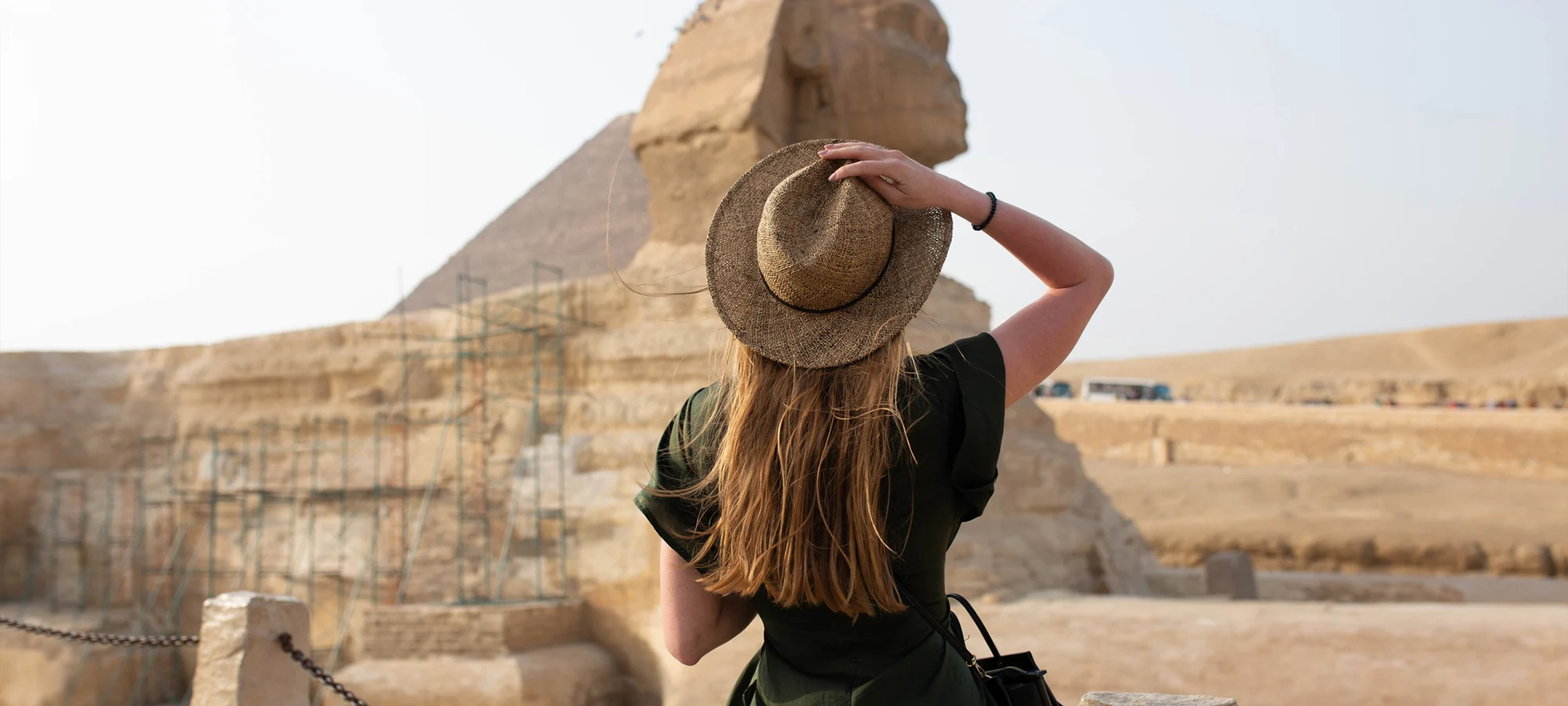 A girl in black dress and a hat standing in front of pyramids