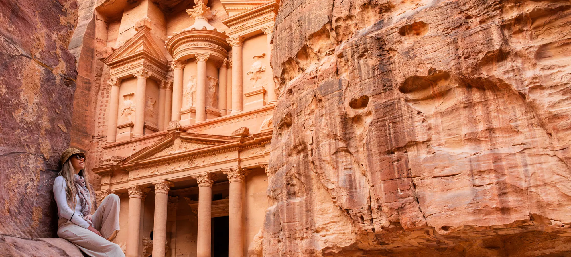 a blonde tourist happily standing in fornt of petra in jordan