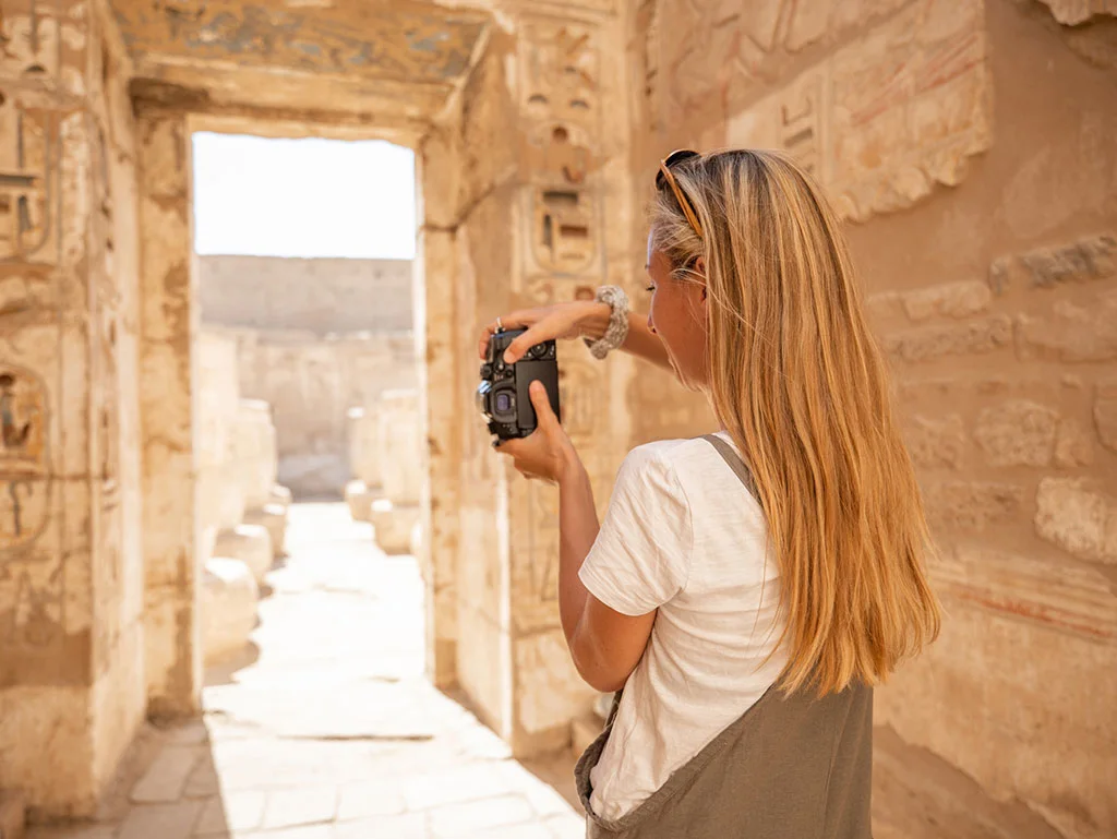 A blond Girl in whit shirt is taking a photo in an ancient egyptian temple