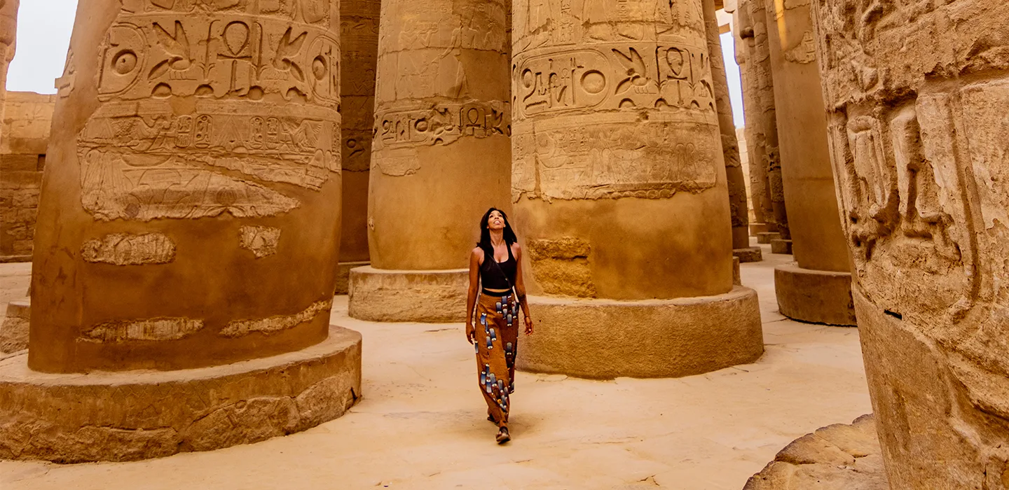 a girl in black shirt and printed pants walking happily in an incient egyptian temple 