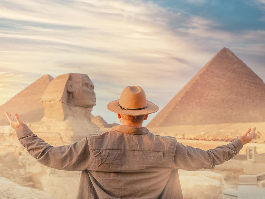 a happy traveller with a hat infront of pyramids if Giza
