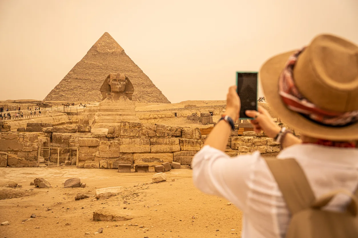 woman standing in front of the pyramids of giza capturing a photo of them, 10 Days Egypt Tour — Cairo, Nile Cruise, Hurghada & Alexandria