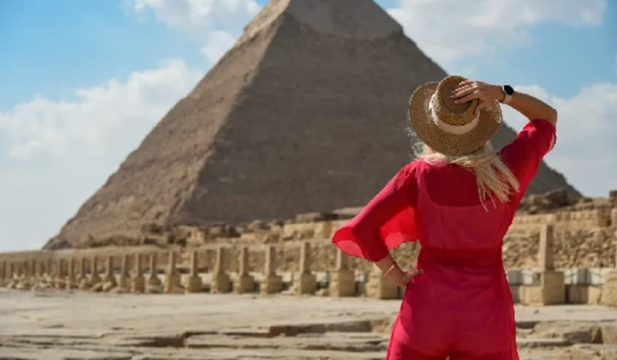Una chica con vestido rojo contempla una pirámide egipcia.