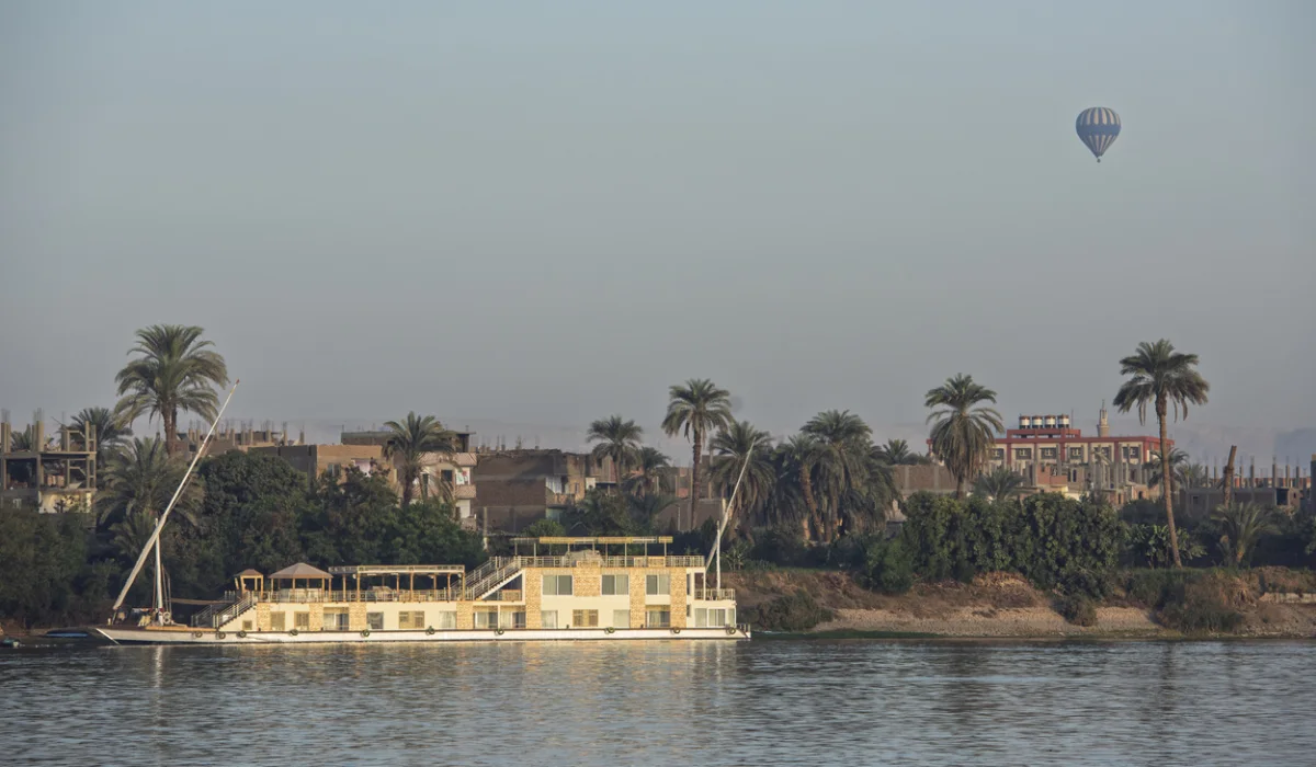 Large luxury traditional Egyptian dahabeya river cruise boat moored on the Nile bank with hot air balloon flying in background