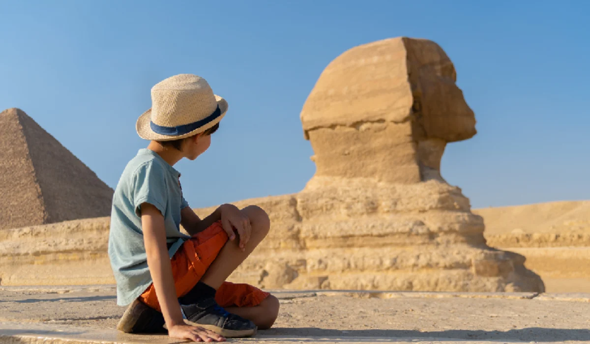 The boy in hat sits in front of the sphinx