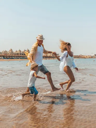 Una familia elegante de verano camina de la mano por una playa paradisíaca tropical al atardecer y disfruta de sus vacaciones.