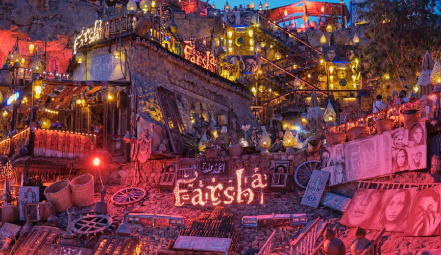 Vista del café Farsha con iluminación nocturna de luces rojas y faroles amarillos.