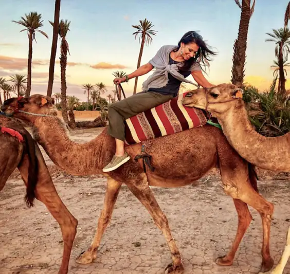 Una donna sorridente cavalca un cammello al tramonto nel deserto fuori Marrakech, Viaggio in Marocco