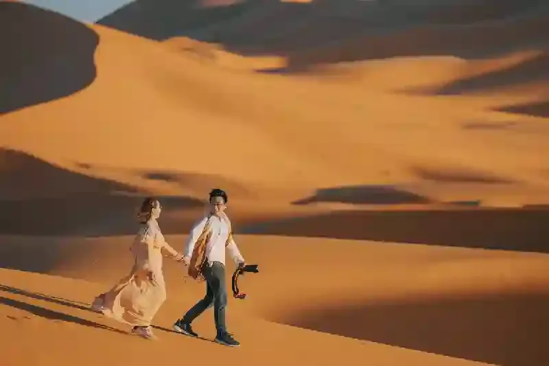 Una coppia cinese asiatica che si tiene per mano camminando nel deserto del Sahara in Marocco, Deserto del sahara marocco