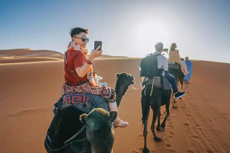 una turista su una carovana di cammelli che attraversa il deserto del Sahara in Marocco, zagora marocco