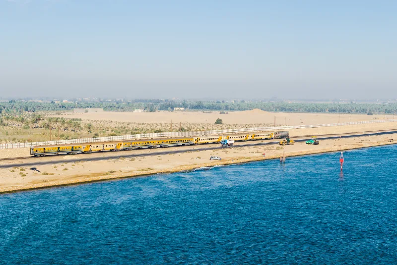 Vista panorámica del lado occidental del Canal de Suez, con un tren de pasajeros, automóviles, camiones y maquinaria para la construcción de carreteras.