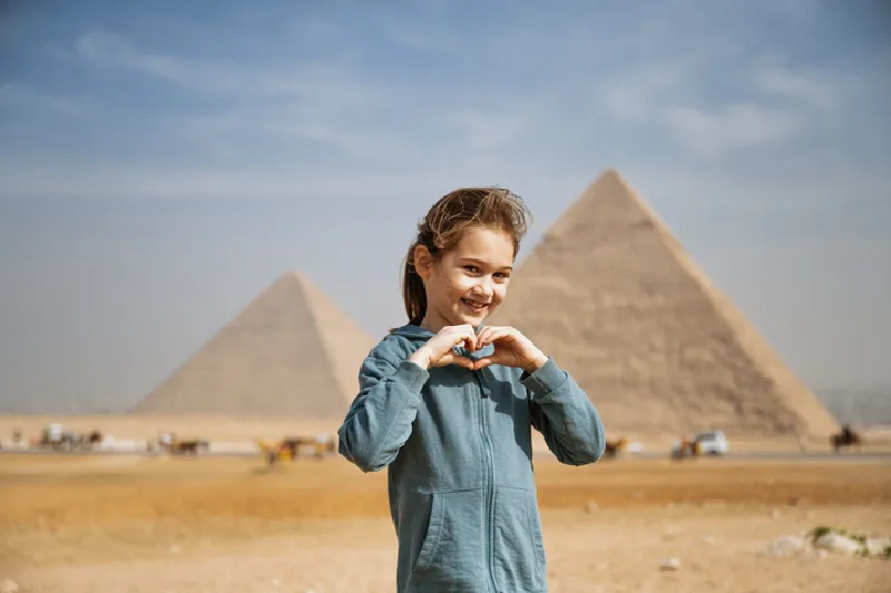 Las majestuosas pirámides de Giza bajo un cielo azul claro, con turistas y camellos caminando por las arenas del desierto en primer plano.