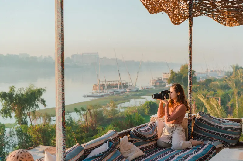 Joven sentada en una terraza y fotógrafo Nilo al atardecer en Luxor