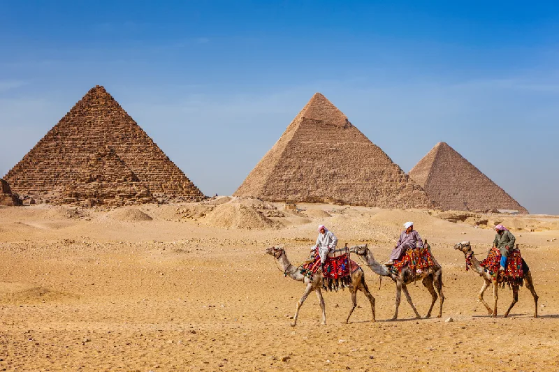 Beduinos montando en camello, pirámides al fondo, Giza, Egipto.