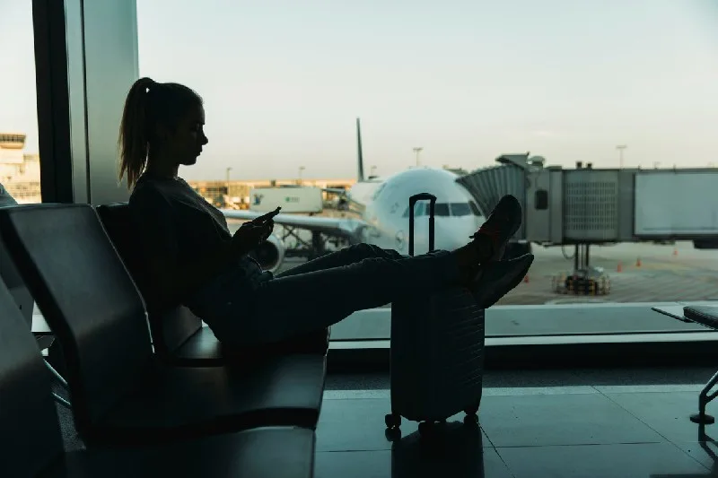 Mujer esperando en el aeropuerto con maleta y avión al fondo