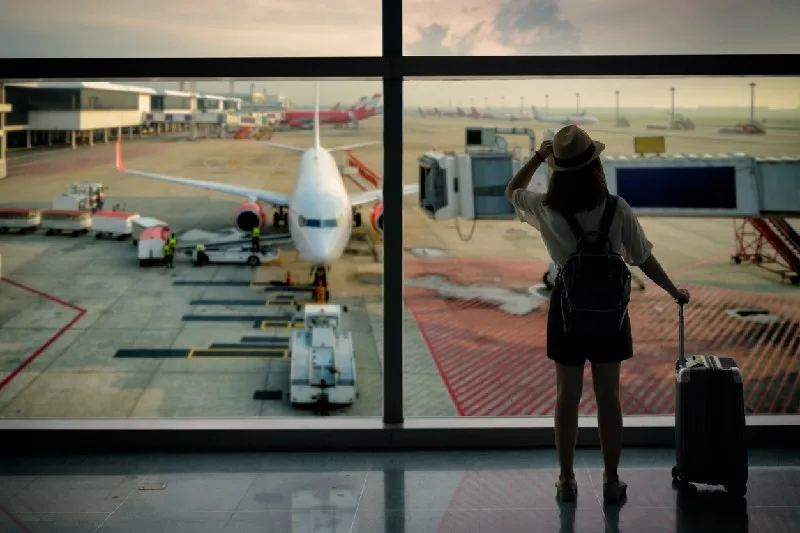Persona de espaldas con maleta en aeropuerto mirando un avión listo para despegar