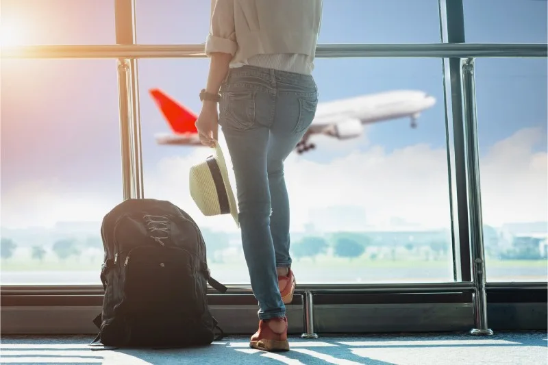 Mujer con mochila y sombrero mirando un avión desde el aeropuerto.
