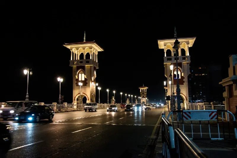 Tráfico nocturno cruzando un puente icónico en Alejandría con luces iluminando la ciudad