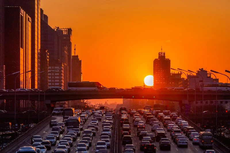 Vista de la autopista de El Cairo con tráfico intenso al atardecer, edificios y el sol en el horizonte.