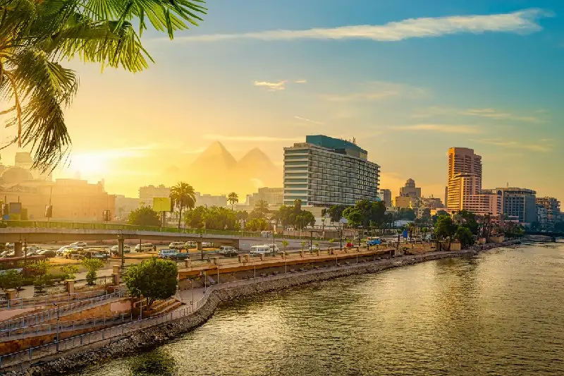 Ciudad de El Cairo al atardecer con tráfico, el río Nilo y las Pirámides en el fondo.