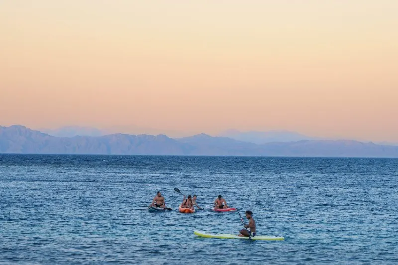 Personas practicando kayak y paddle en el Mar Rojo, en Dahab, Egipto, al atardecer.