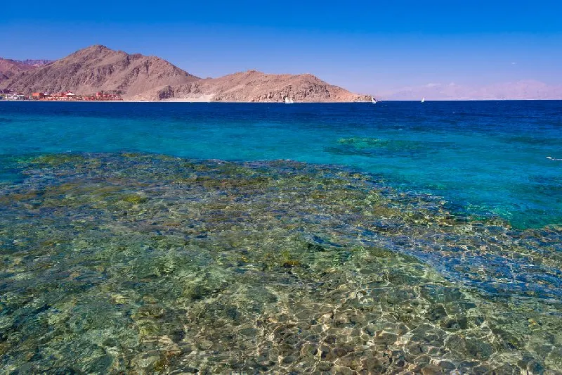 Aguas cristalinas del Mar Rojo en Dahab, Egipto, con montañas de fondo.