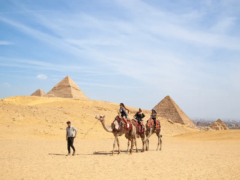 Gruppo di turisti in cammello nel deserto con le Piramidi di Giza sullo sfondo