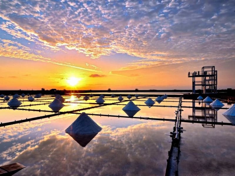 White salt mounds glisten under a golden sunset at one of Taiwan's oldest salt fields, a 300-year-old coastal wonder where visitors can experience traditional salt-harvesting methods firsthand.