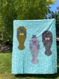 Woollypetals Manatee Migration quilt hanging outdoors with three manatees