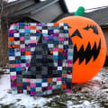 Woollypetals Something Wicked Quilt displayed with giant orange jack-o'-lantern decoration