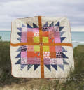 Woollypetals Wash Your Paws quilt displayed on beach with ocean backdrop