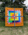 Woollypetals Wash Your Paws quilt displayed outdoors with colorful star blocks on orange background