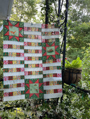 Woollypetals StarBeam Quilt hanging outdoors with red and green holiday fabrics